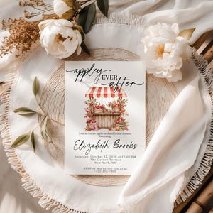 Puede incluir: Una tarjeta de invitaci&oacute;n rectangular para una despedida de soltera con el texto 'appley EVER after' sobre una ilustraci&oacute;n en acuarela de un puesto de manzanas. La tarjeta incluye detalles para Elizabeth Brooks el 13 de octubre de 2026 en Nueva York.
