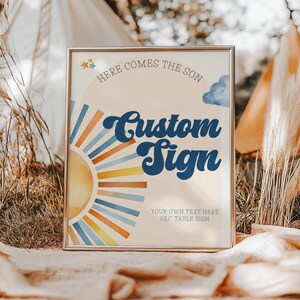 May include: A framed sign with the text "Here Comes the Son" and "Custom Sign" in a retro font. The design includes a watercolor sunburst in yellow, orange, and blue hues. The sign is 5x7 inches and suitable for a table.