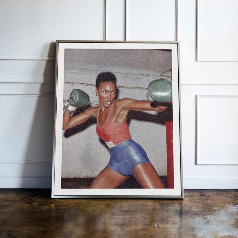 May include: Framed print depicting a person in a boxing pose, wearing a red vest, blue shorts, and green boxing gloves. The image has a vintage style, with a neutral background and a red boxing post.