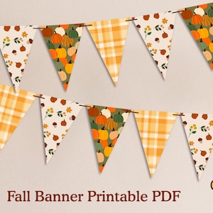 Puede incluir: Un estandarte con banderines triangulares con temática otoñal. Los banderines presentan patrones de calabazas, hojas de otoño y cuadros en naranja, amarillo y verde. El estandarte está ensartado en una fina cuerda marrón.