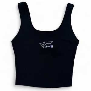 Könnte beinhalten: Schwarzes geripptes Tanktop mit weiß gestickter Umrisslinie einer Rennstrecke und dem Wort "Austin" in Schreibschrift. Eine kleine amerikanische Flagge ist neben dem Wort "Austin" gestickt. Das Tanktop hat einen Rundhalsausschnitt und breite Träger.