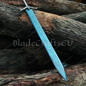 K&ouml;nnte beinhalten: Ein gro&szlig;es, verziertes Schwert mit einer blauen Klinge und einem silbernen Griff liegt auf einem Holzstapel. Die Klinge weist ein detailliertes Muster auf. Der Text "BladeCraftsEU" ist im Bild sichtbar.