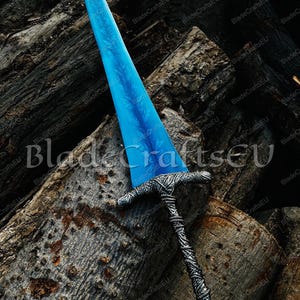K&ouml;nnte beinhalten: Ein Fantasy-Schwert mit einer leuchtend blauen Klinge mit detailliertem floralem Muster. Der Knauf und der Griff sind silberfarben mit aufwendigen Webmustern. Das Schwert liegt auf einem Stapel verwitterter Baumst&auml;mme.
