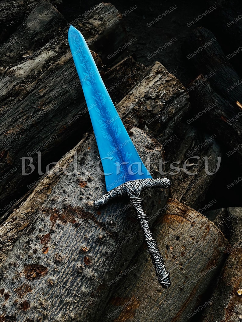 K&ouml;nnte beinhalten: Ein Fantasy-Schwert mit einer leuchtend blauen Klinge mit detailliertem floralem Muster. Der Knauf und der Griff sind silberfarben mit aufwendigen Webmustern. Das Schwert liegt auf einem Stapel verwitterter Baumst&auml;mme.