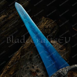 K&ouml;nnte beinhalten: Ein mittelalterlich anmutendes Schwert mit einer leuchtend blauen Klinge, verziert mit einem ge&auml;tzten Blattmuster. Der Griff ist aufwendig mit einer silbernen Oberfl&auml;che gestaltet. Das Schwert wird vor einem dunklen, strukturierten Hintergrund pr&auml;sentiert.