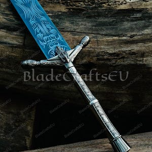 K&ouml;nnte beinhalten: Ein Fantasy-Schwert mit einer blauen Klinge und einem verzierten silbernen Griff. Die Klinge weist aufwendige ge&auml;tzte Designs auf. Der Griff hat einen detaillierten Parier und Knauf. Das Schwert wird vor einem Holzgrund gezeigt. Der Text "BladeCraftsEU" ist sichtbar.