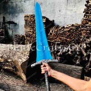 K&ouml;nnte beinhalten: Ein gro&szlig;es, blaues Schwert mit dekorativer Klinge und gemustertem Griff. Das Schwert wird vor einem Hintergrund aus Holz und Baumst&auml;mmen gehalten. Der Text "BladeCraftsEU" ist auf dem Bild sichtbar.