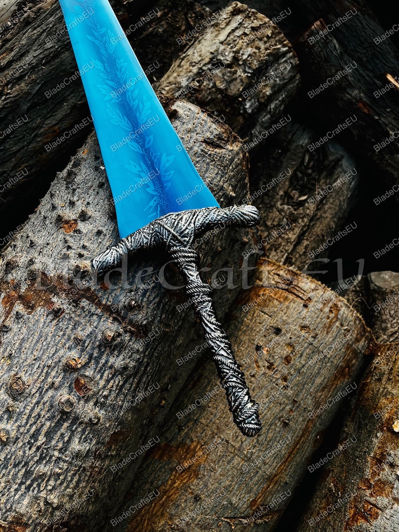 K&ouml;nnte beinhalten: Ein Fantasy-Schwert mit einer leuchtend blauen Klinge und einem detaillierten silberfarbenen Griff. Die Klinge hat ein dekoratives Muster. Das Schwert liegt auf einem Stapel Holzscheite und bildet einen rustikalen Hintergrund.