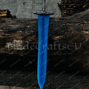 K&ouml;nnte beinhalten: Ein gro&szlig;es, blaues Fantasy-Schwert mit detailliertem silbernen Griff und Parierstange. Die Klinge hat ein geschwungenes Design mit ge&auml;tzten floralen Mustern. Das Schwert wird vor einem Hintergrund aus verwittertem Holz und dem Text "BladeCraftsEU" pr&auml;sentiert.