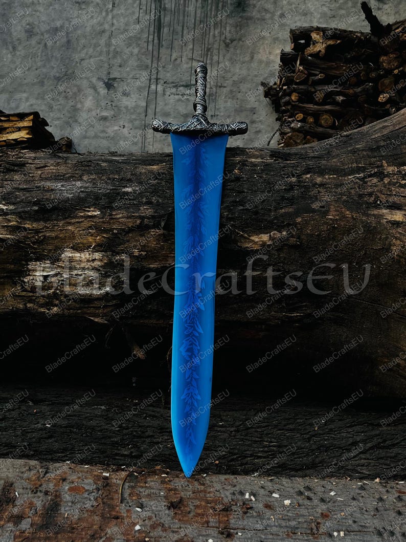 K&ouml;nnte beinhalten: Ein gro&szlig;es, blaues Fantasy-Schwert mit detailliertem silbernen Griff und Parierstange. Die Klinge hat ein geschwungenes Design mit ge&auml;tzten floralen Mustern. Das Schwert wird vor einem Hintergrund aus verwittertem Holz und dem Text "BladeCraftsEU" pr&auml;sentiert.