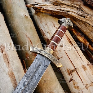 Può includere: Immagine dettagliata di una spada con una lama decorata e un'impugnatura in legno. L'impugnatura è marrone con dettagli dorati. La spada è posta su uno sfondo di tronchi di legno. Il testo "Blade Crafts EU" è visibile.