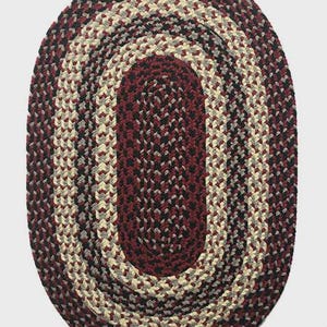 May include: Oval braided rug in shades of burgundy, black, gray, and cream. The rug features a central burgundy oval, surrounded by concentric braids of mixed colors. A decorative floor covering.