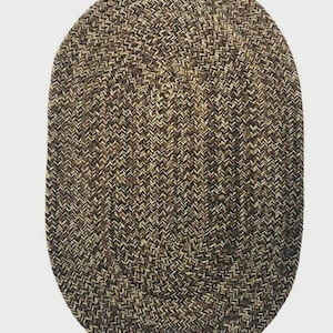 May include: Oval braided rug in shades of brown, tan, and black. The rug has a textured surface with a woven pattern. The rug is designed for indoor use and is suitable for a living room or bedroom.