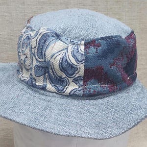 May include: A light blue bucket hat with a patterned band. The band features a floral design in white and blue, and a section with a dark blue and burgundy pattern. The hat has a wide brim.