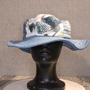 May include: A blue and white bucket hat with a wide brim. The hat features a patterned design with birds and foliage on the crown. The brim and the band around the crown are a solid light blue color.