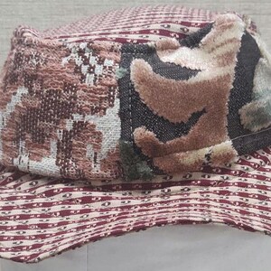 May include: A patterned bucket hat with a wide brim. The hat features a mix of textures and patterns, including a burgundy and white striped brim and a crown with a patchwork design in shades of brown, beige, and black.