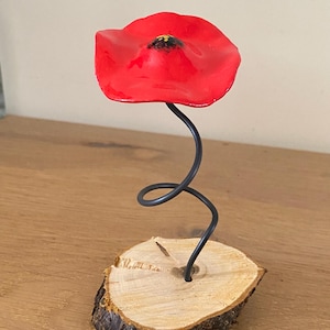 Peut inclure: Sculpture d'un coquelicot rouge avec un centre noir, monté sur une tige en métal noir torsadée. La tige est fixée à une petite base ronde en bois naturel, pour la décoration.