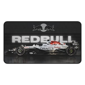 May include: A rectangular desk mat featuring a side profile of a white, black, and red Formula 1 race car. The background is dark gray with the text REDBULL in large white letters and the Red Bull logo centered above the car. Various sponsor logos including Oracle, Honda, and Mobil 1 are visible on the car body.