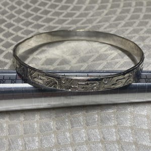 Peut inclure: Un bracelet jonc argenté avec un motif gravé. Le bracelet circulaire est en métal. Le motif gravé est visible sur toute la circonférence. Le bracelet mesure environ 6,5 cm de diamètre.