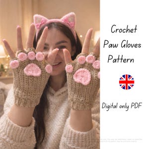 May include: Crochet paw gloves pattern. The image shows a pair of brown fingerless gloves with pink paw pads. The gloves are handmade and feature a cat paw design. A pink cat ear headband is also visible. The text "Crochet Paw Gloves Pattern" is displayed.