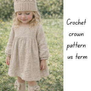 May include: A child in a beige crochet crown, dress, and knee-high socks with bow details. The dress has long sleeves and a gathered skirt. The image includes the text "Crochet crown pattern us term."