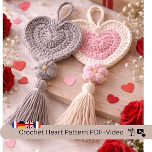 May include: Two handmade crochet heart decorations. One is grey, the other is pink and white. Each has a flower and tassel. The text "Crochet Heart Pattern PDF+Video" is at the bottom of the image.