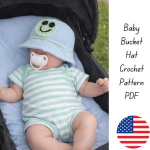 May include: A baby wearing a light blue crochet bucket hat with a green smiley face and a matching light blue trim. The baby is also wearing a striped green and white onesie. Text on the right says "Baby Bucket Hat Crochet Pattern PDF".