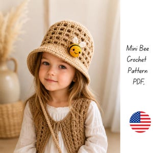 May include: A beige crochet bucket hat featuring a small, round, yellow and black bee appliqu&eacute; with white wings. The hat has a grid-like openwork pattern on the crown and a solid brim. Text on the right reads Mini Bee Crochet Pattern PDF.
