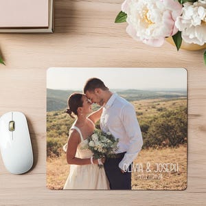 May include: A rectangular mousepad featuring a wedding photo of a couple embracing outdoors. The mousepad has the names "OLIVIA & JOSEPH" and the date "07.12.2025" printed on it. A white computer mouse is visible on the left.