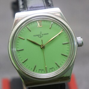May include: A vintage Ulysse Nardin wristwatch with a bright green dial and gold hands. The watch has a silver-coloured case and a black leather strap. The dial features the brand name and the words "Swiss Made".
