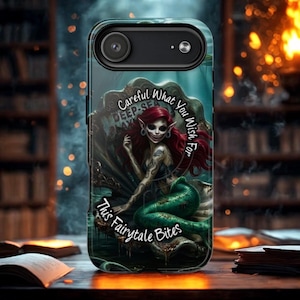 May include: A smartphone case featuring a graphic of a red-haired mermaid with a green tail sitting inside a large seashell. The text reads, Careful What You Wish For, This Fairytale Bites. The design includes dark, aquatic, and mystical elements.