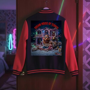May include: A black varsity jacket with red sleeves and striped ribbed cuffs, featuring a large rectangular graphic on the back. The print depicts a house with the text "DREAM HOUSE OF TERROR" and "MR. CREEP-O HEAD" alongside various doll figures.