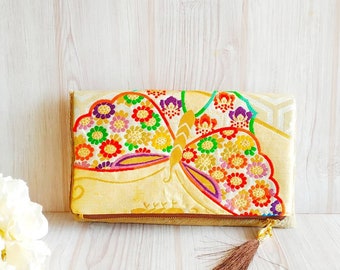 May include: A gold clutch purse with a colorful butterfly design. The purse has a brown tassel zipper pull.