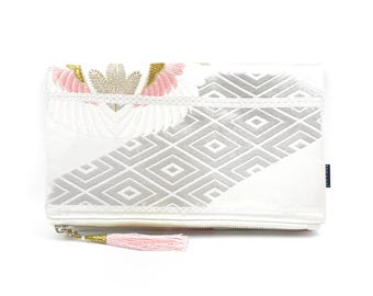 May include: White clutch bag with a pink and gold embroidered design of wings and a geometric pattern. The bag has a pink tassel.