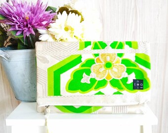 May include: A green and white clutch purse with a floral design and gold accents. The purse has a zipper closure and a tassel.