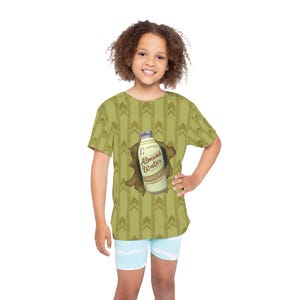 May include: A child wearing a green t-shirt with a repeating arrow pattern. The shirt features a graphic of an almond water bottle bursting through a hole. The text on the bottle reads "Almond Water Original Vanilla & Almond". The child is also wearing light blue shorts.