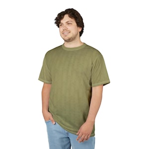 May include: Olive green short-sleeve t-shirt with a subtle pattern. The shirt has a crew neck and is worn with blue jeans. The model is standing in front of a white background.