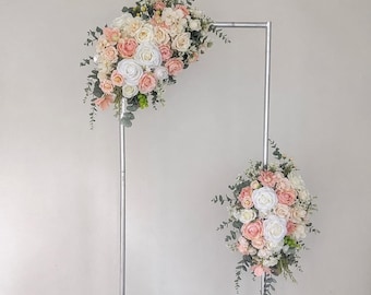 May include: A silver metal wedding arch adorned with bouquets of white, peach, and pink roses, hydrangeas, and foliage. Floral arrangements are positioned at the top and bottom of the arch.