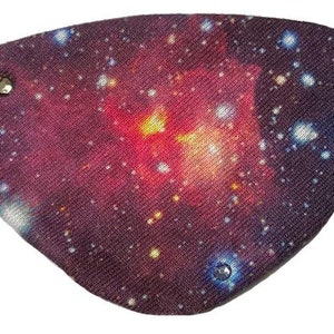 Puede incluir: Un parche para el ojo negro con un estampado de galaxia que presenta una nebulosa roja, naranja y amarilla. El parche tiene tres pedrerías plateadas.