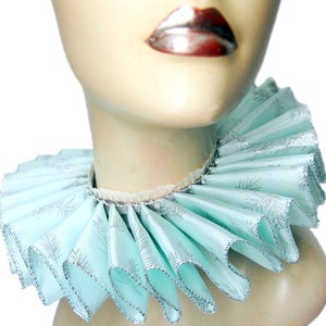 May include: A light blue ruffled collar with a silver glitter pattern. The collar is made of fabric and has a delicate, feminine look.