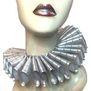 May include: A silver ruffled collar with a subtle plaid pattern. The collar is made of satin ribbon and is designed to be worn around the neck.