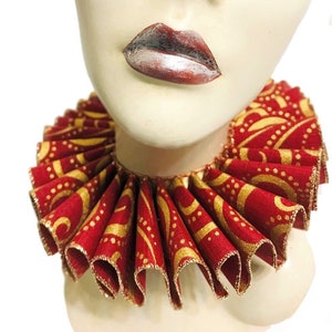 May include: A red and gold ruffled collar with a gold swirl pattern. The collar is made of fabric and has a gold trim.