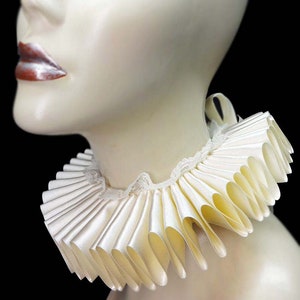 May include: A white satin ruffled collar with a lace trim. The collar is worn on a mannequin's neck.