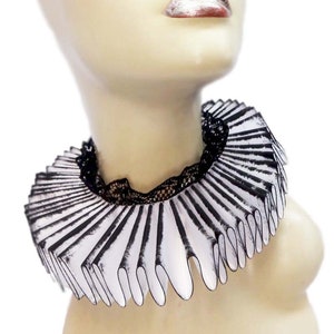 May include: A white and black ruffled collar with a black lace trim. The collar is worn on a mannequin with a white face and red lips.