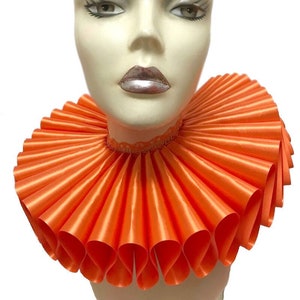 May include: A large, bright orange ruffled collar made of satin. The collar is worn on a mannequin's neck.