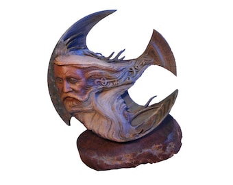 May include: A wooden sculpture of a bearded man's face, carved in a crescent shape, with intricate details and a blue-grey patina. The sculpture is mounted on a natural stone base.