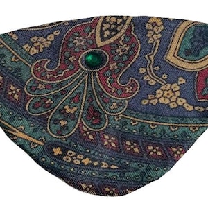 Puede incluir: Un parche para el ojo azul, verde, rojo y dorado con estampado paisley y una joya verde en el centro.