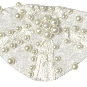 May include: A white satin eye patch featuring a cluster of round white faux pearls in the center, accented with scattered individual pearls across the fabric surface and a tan elastic strap attached to both sides for secure placement.