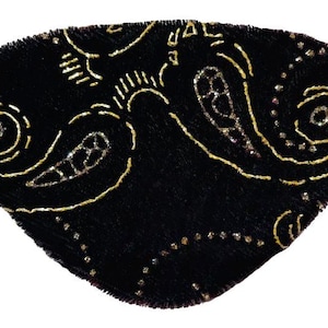 Könnte beinhalten: Ein schwarzes Augenpflaster mit einem goldenen Paisley-Muster und goldenen Glitzerakzenten.