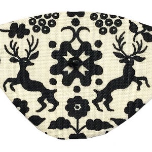 Puede incluir: Una máscara para los ojos de tela blanca con un patrón blanco y negro de ciervos estilizados, flores y formas geométricas. La máscara para los ojos tiene una cinta elástica negra.
